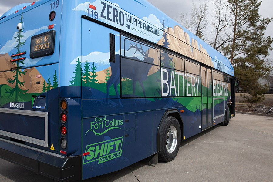 A colorfully painted electric bus with zero tailpipe emissions sits idle in a parking lot.