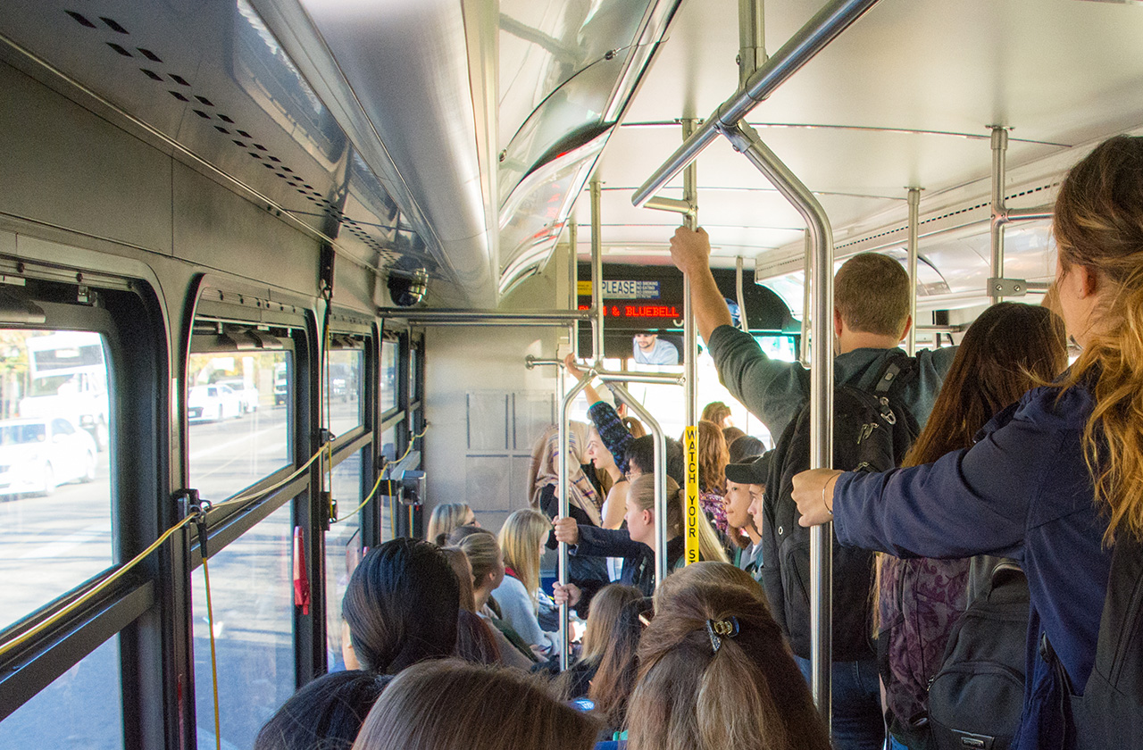 people riding on a bus, some standing up holding pole to balance