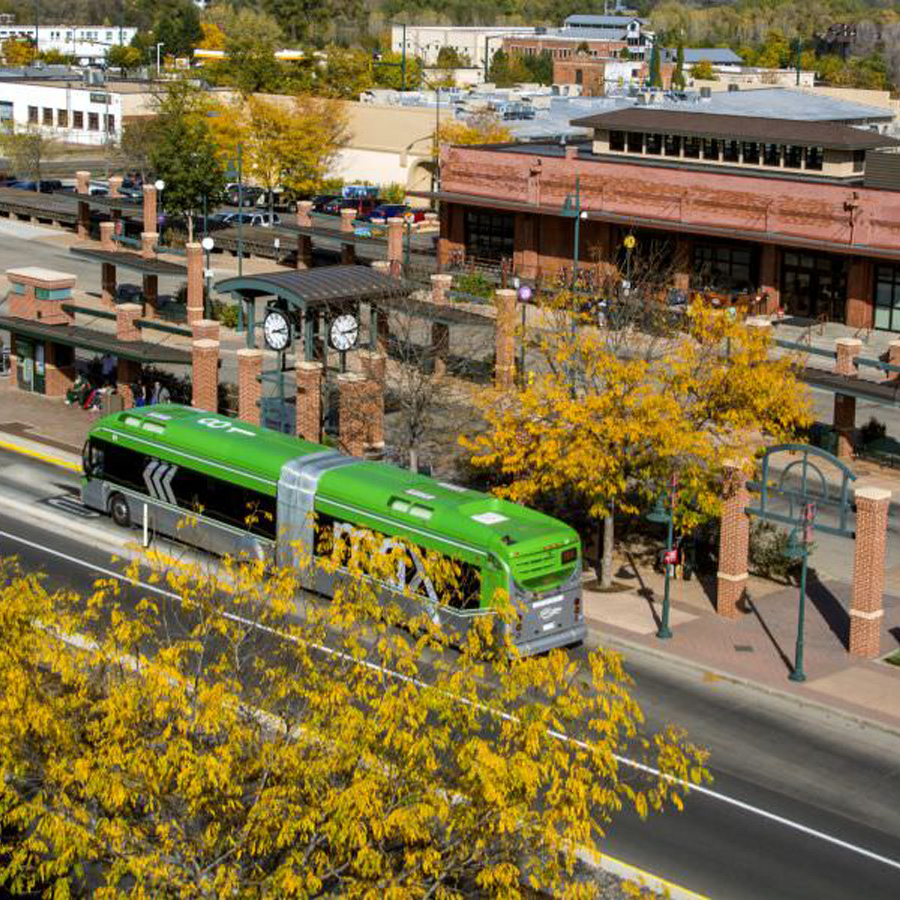 green bus driving on street outside of bus station on a fall day