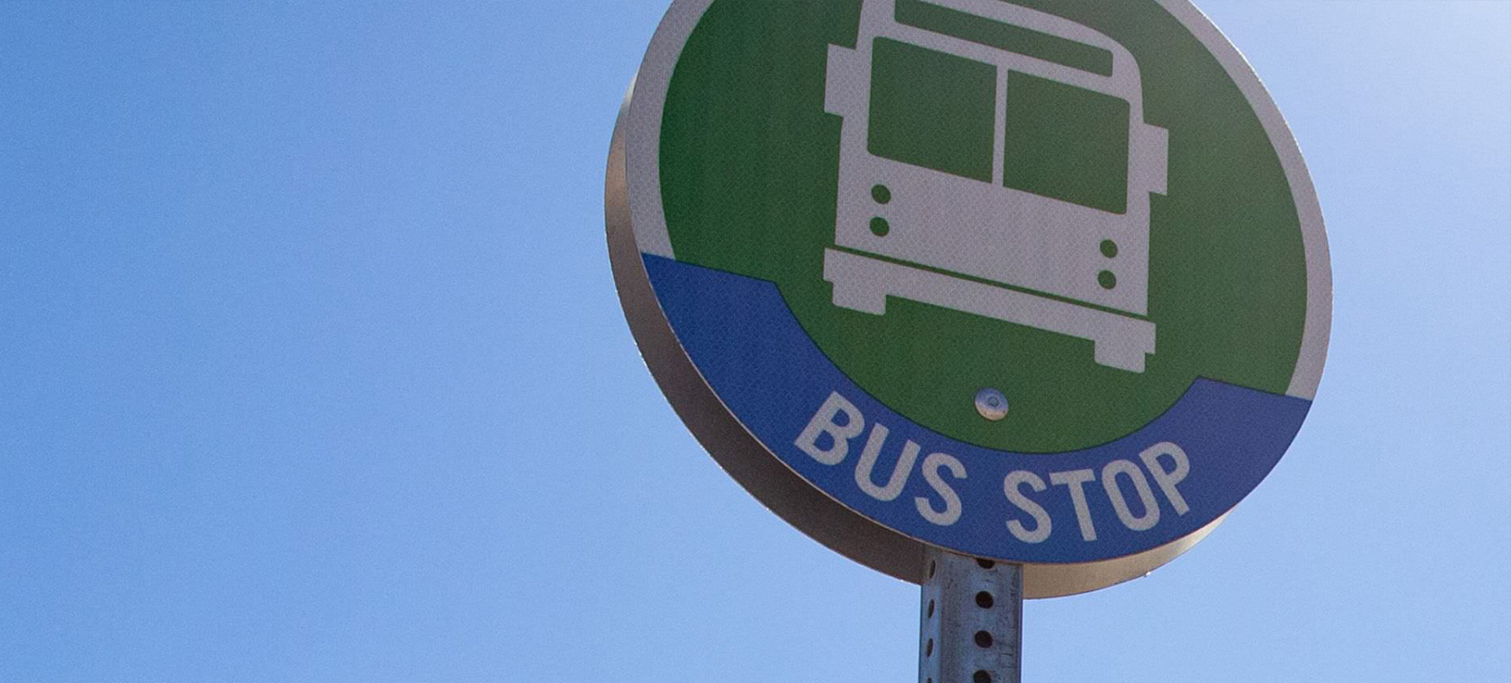 A bus stop sign rests against a clear, blue sky. 