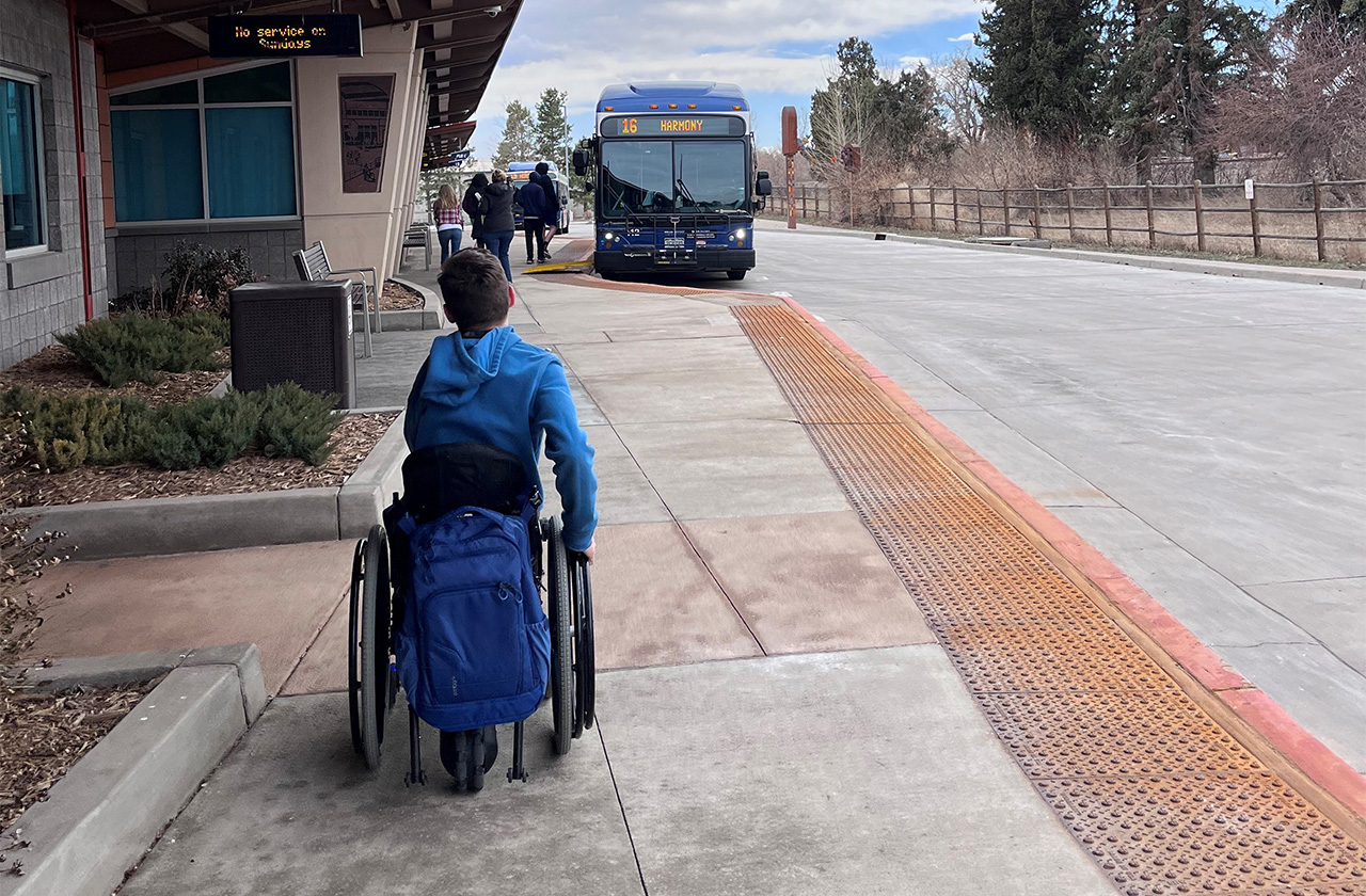 boy in a wheelchair outside of bus station with bus coming towards them