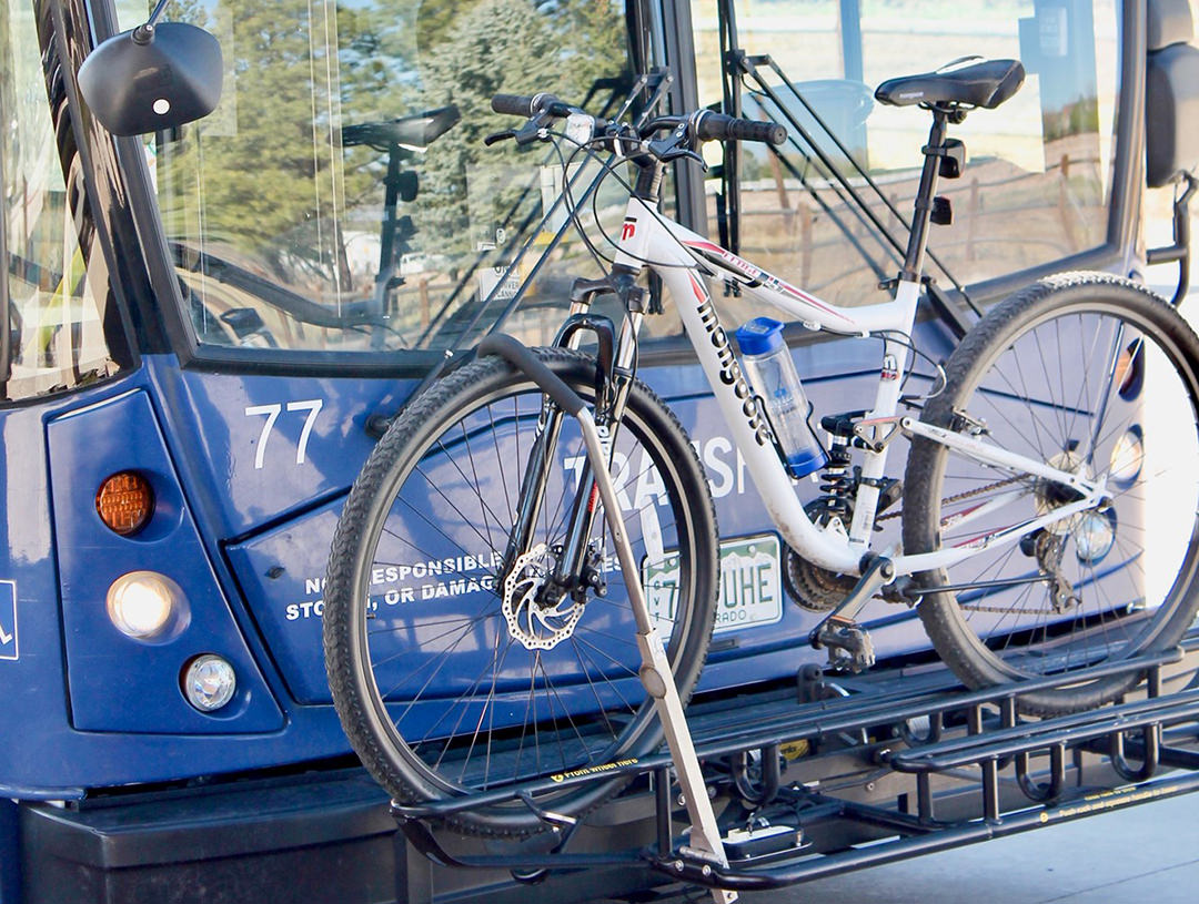 A white bike is attached to a bike rack on the front of a bus.