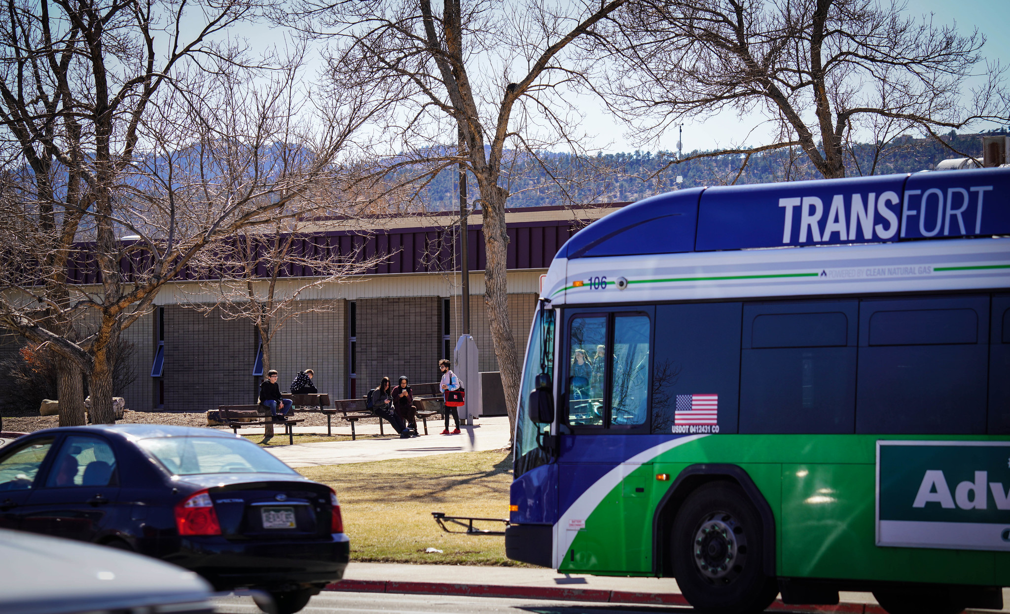 Transfort bus with cars in traffic driving passing by a school.